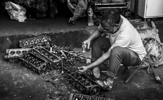 Man working on car engine parts outdoors.
